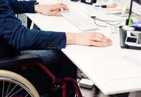 Hombre en silla de ruedas frente a un ordenador en su puesto de trabajo | Foto de 123FR / Nullplus